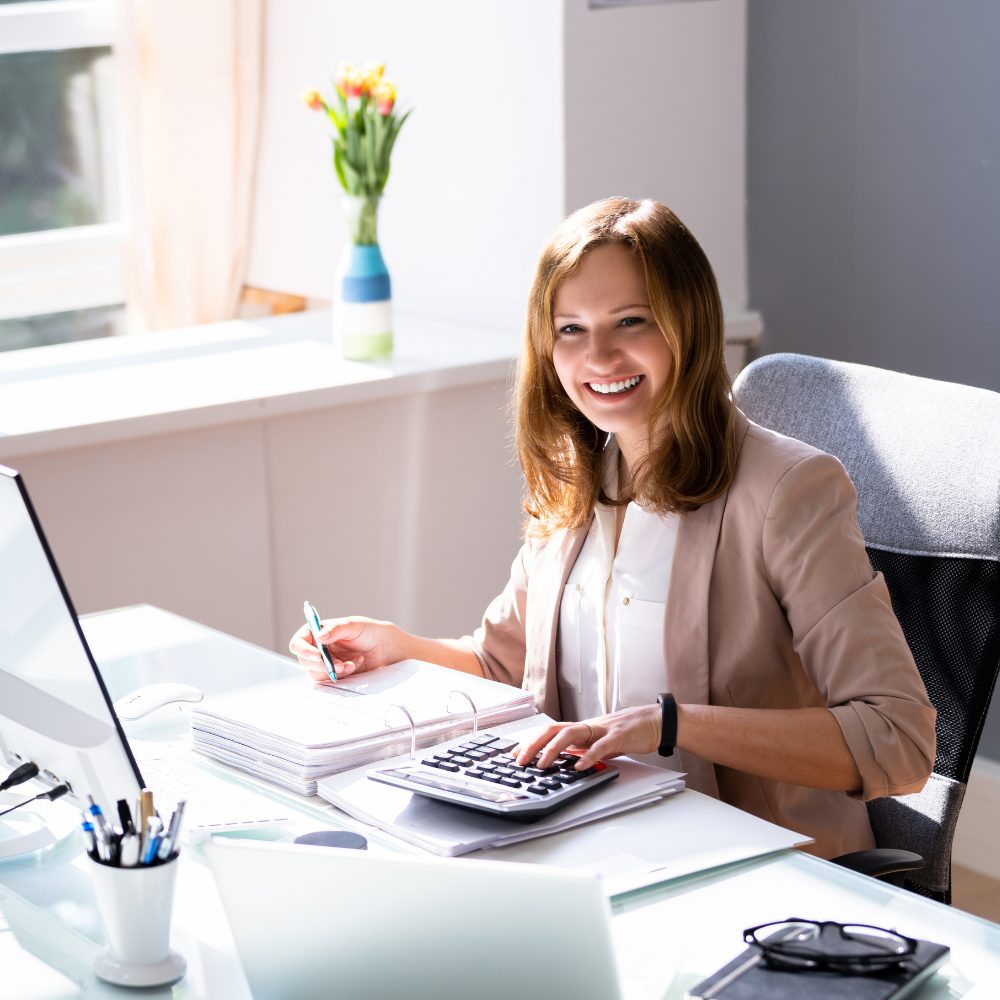 An accountant reviewing an invoice on a monitor while working at a desk with a calculator and documents.